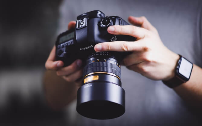 Close up of a person's hands holding a Cannon camera at waist level, with the display facing towards their face