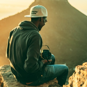 Profile photo of a contributor, sitting among rocks, facing a mountain range at sunset, with a camera in hand